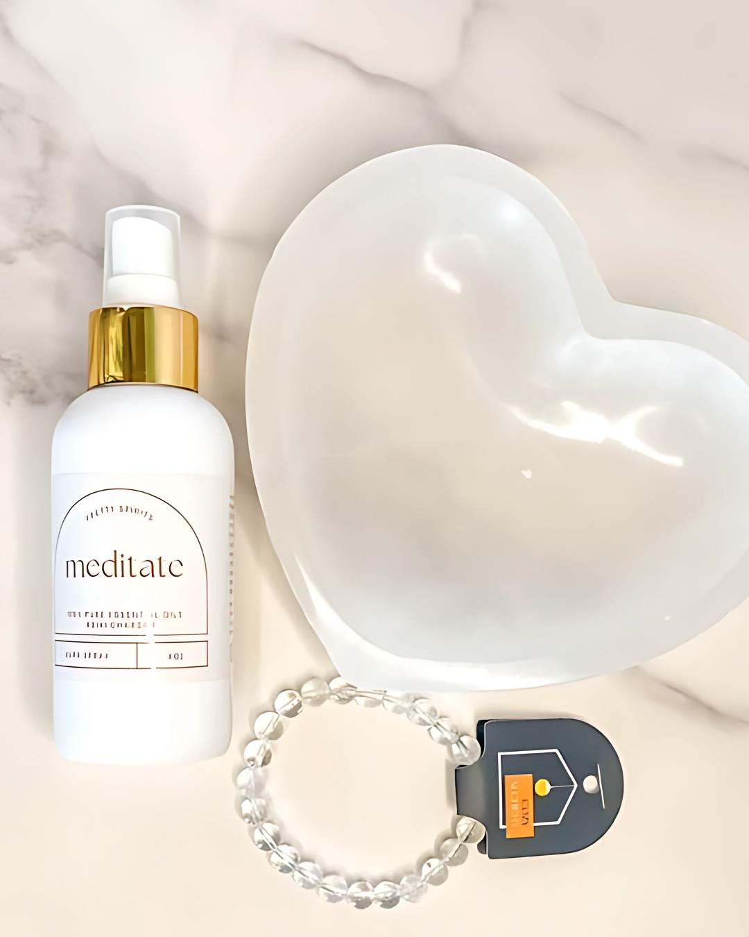 White bottle labeled 'meditate', heart-shaped object, bracelet, and small device on a light background