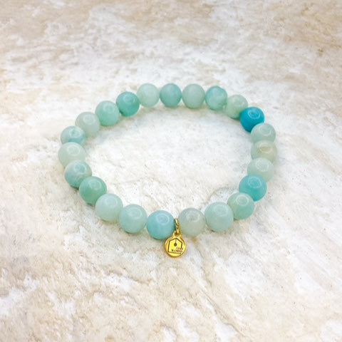 Beaded bracelet with a gold charm on a textured beige surface