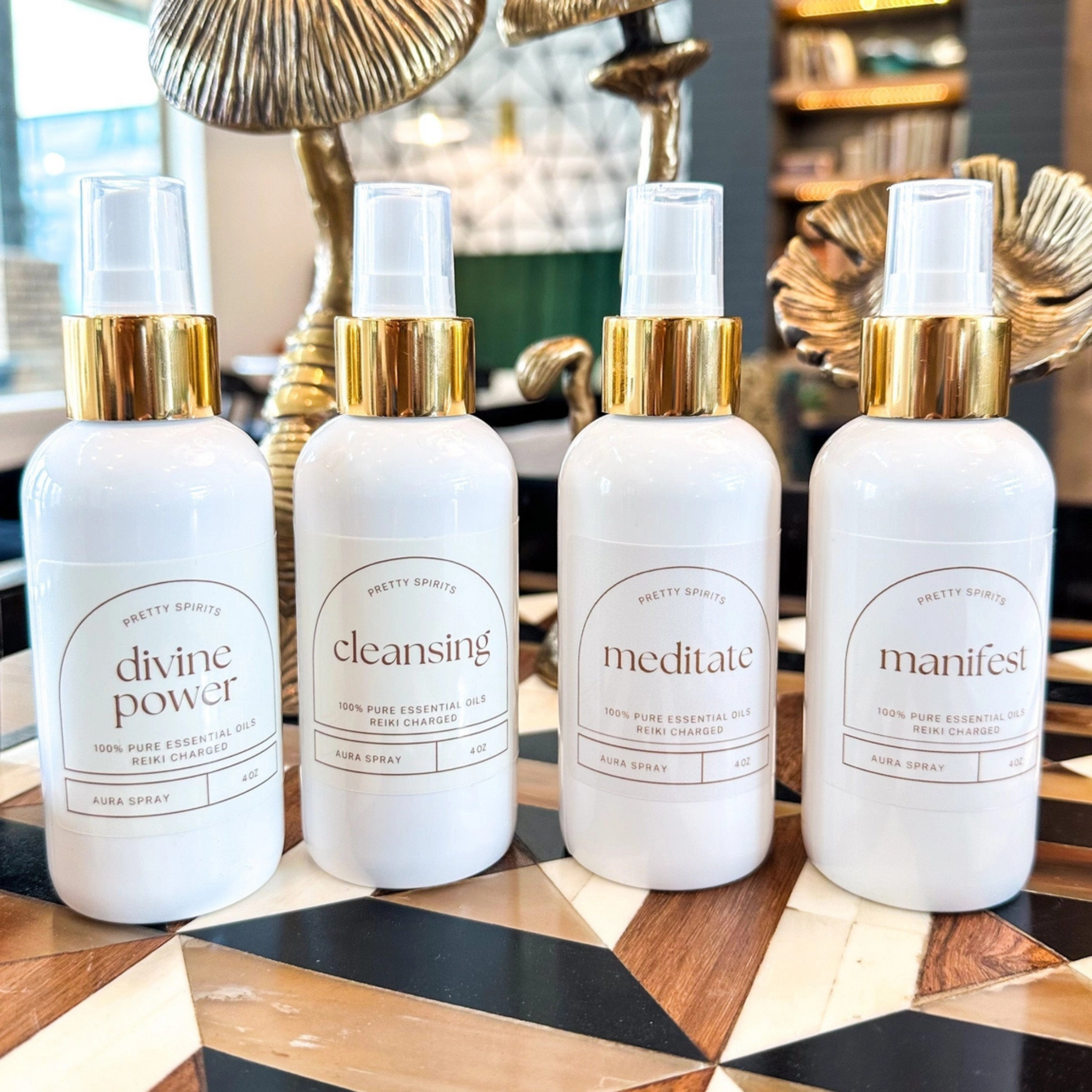 Four white spray bottles with gold caps on a decorative surface.