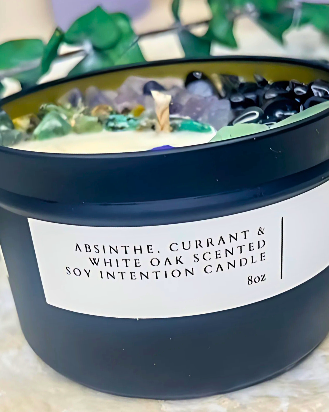 Scented candle with a label indicating 'Absinthe, Currant & White Oak' fragrance and 'Soy Intention Candle' on a neutral background.