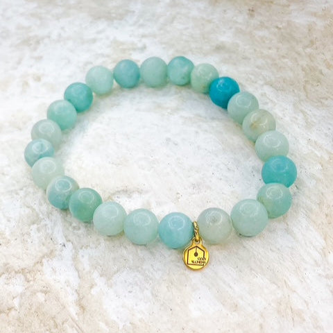 Turquoise beaded bracelet with a gold Buddha charm on a textured white surface