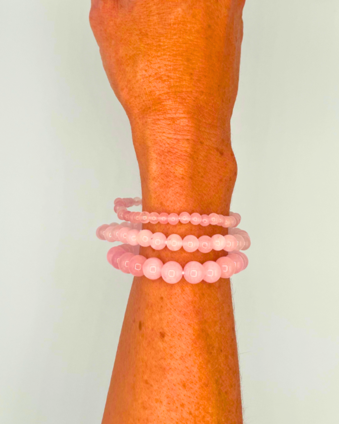 Wrist wearing two pink beaded bracelets on a plain background