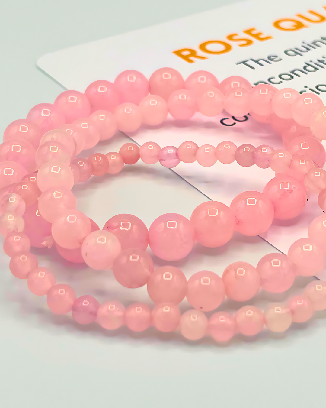 Pink beaded bracelets on a light gray background with a card partially visible.