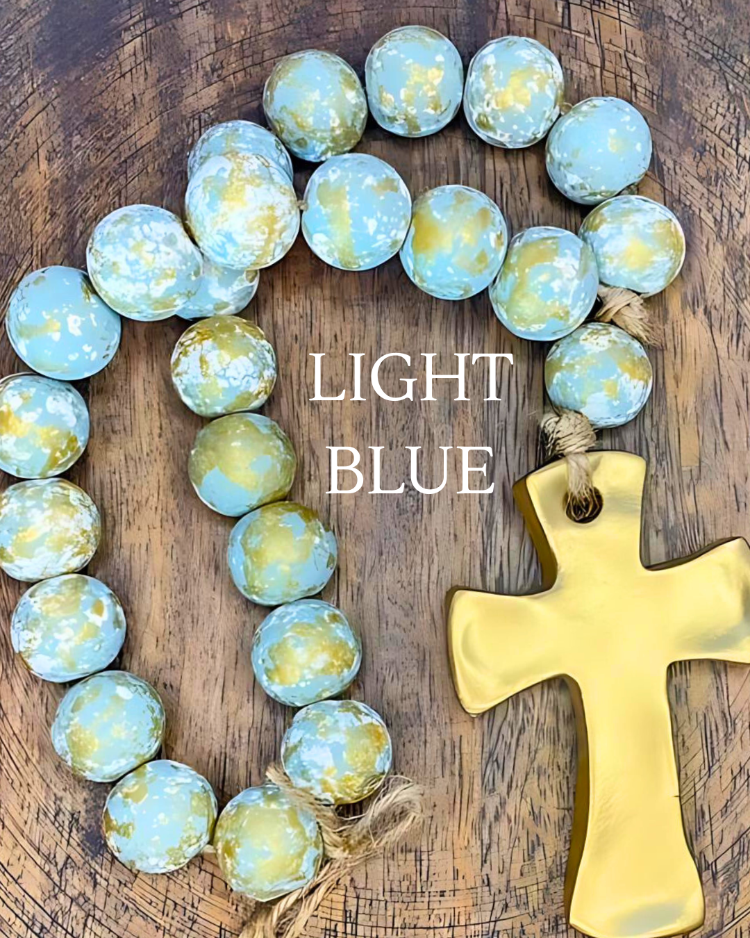 Decorative wreath with light blue marbled stones and a gold cross on a wooden background