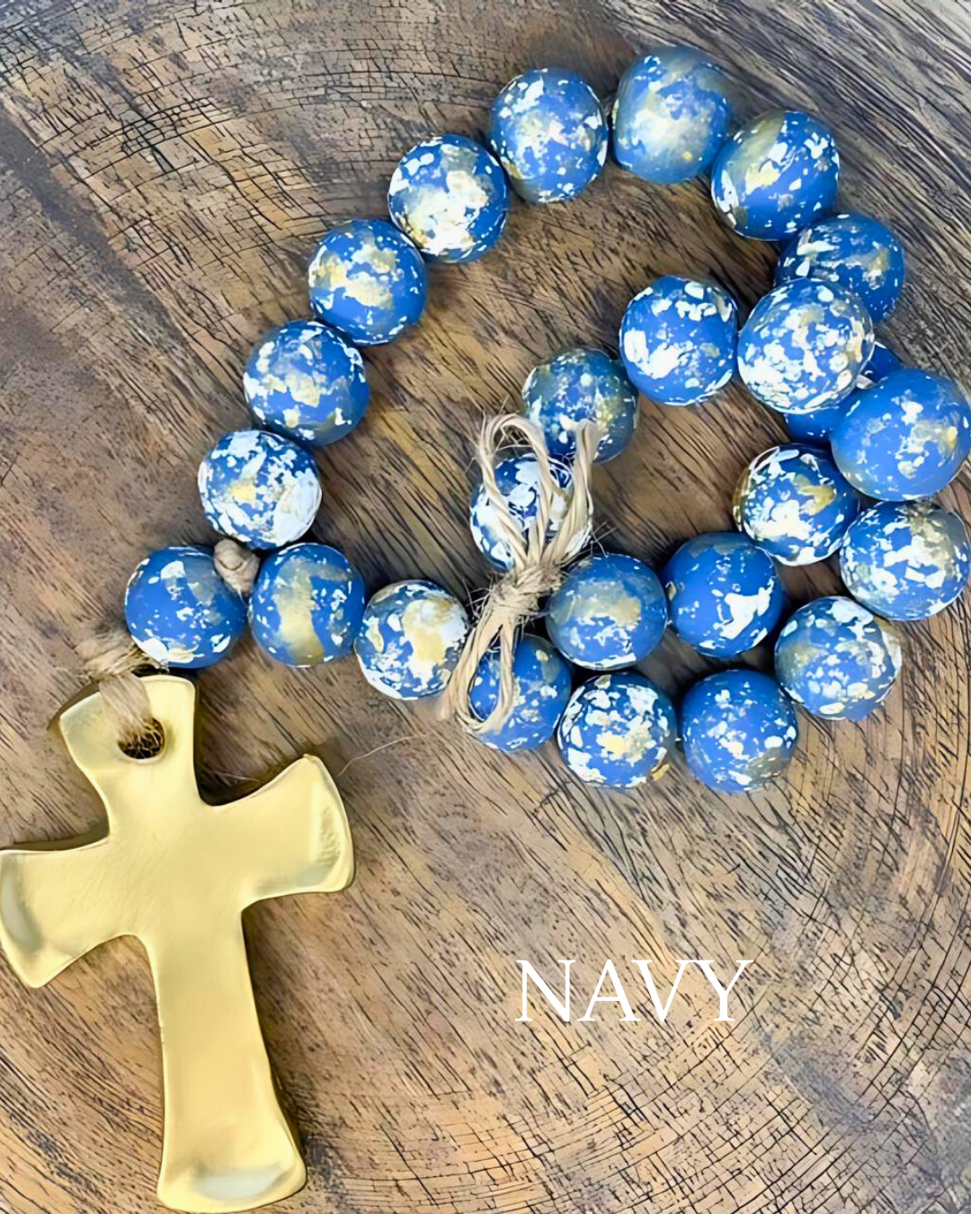 Blue and white speckled beaded necklace with a gold cross on a wooden surface, labeled 'NAVY'.