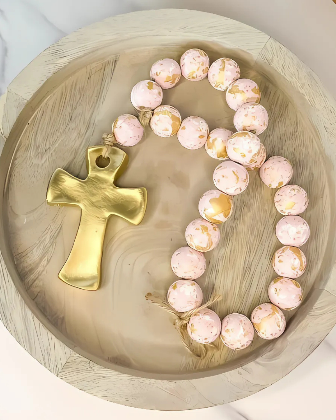 Bracelet with pink beads and a gold cross on a wooden surface