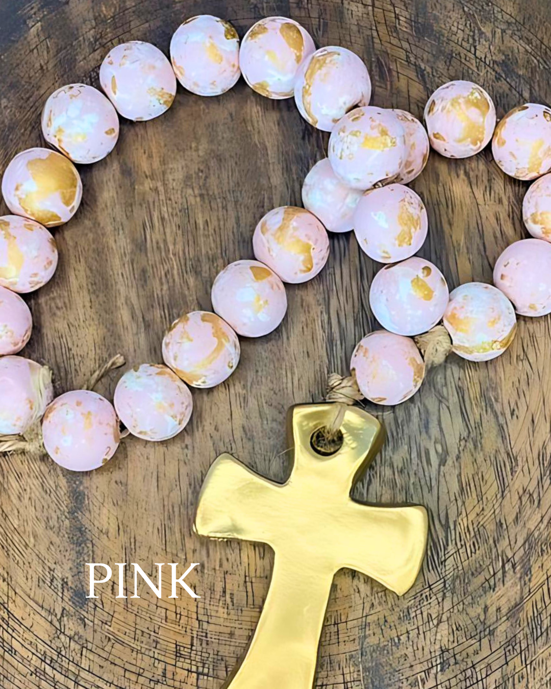 Pink and gold rosary with a gold cross on a wooden surface