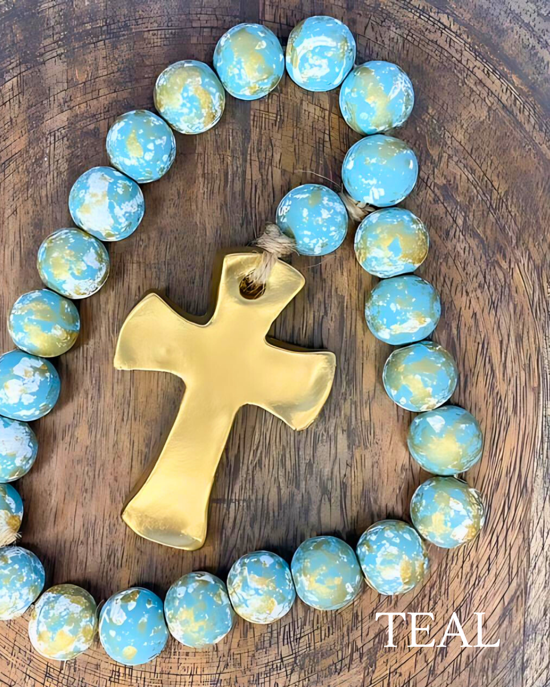 Teal and gold rosary with a gold cross on a wooden surface