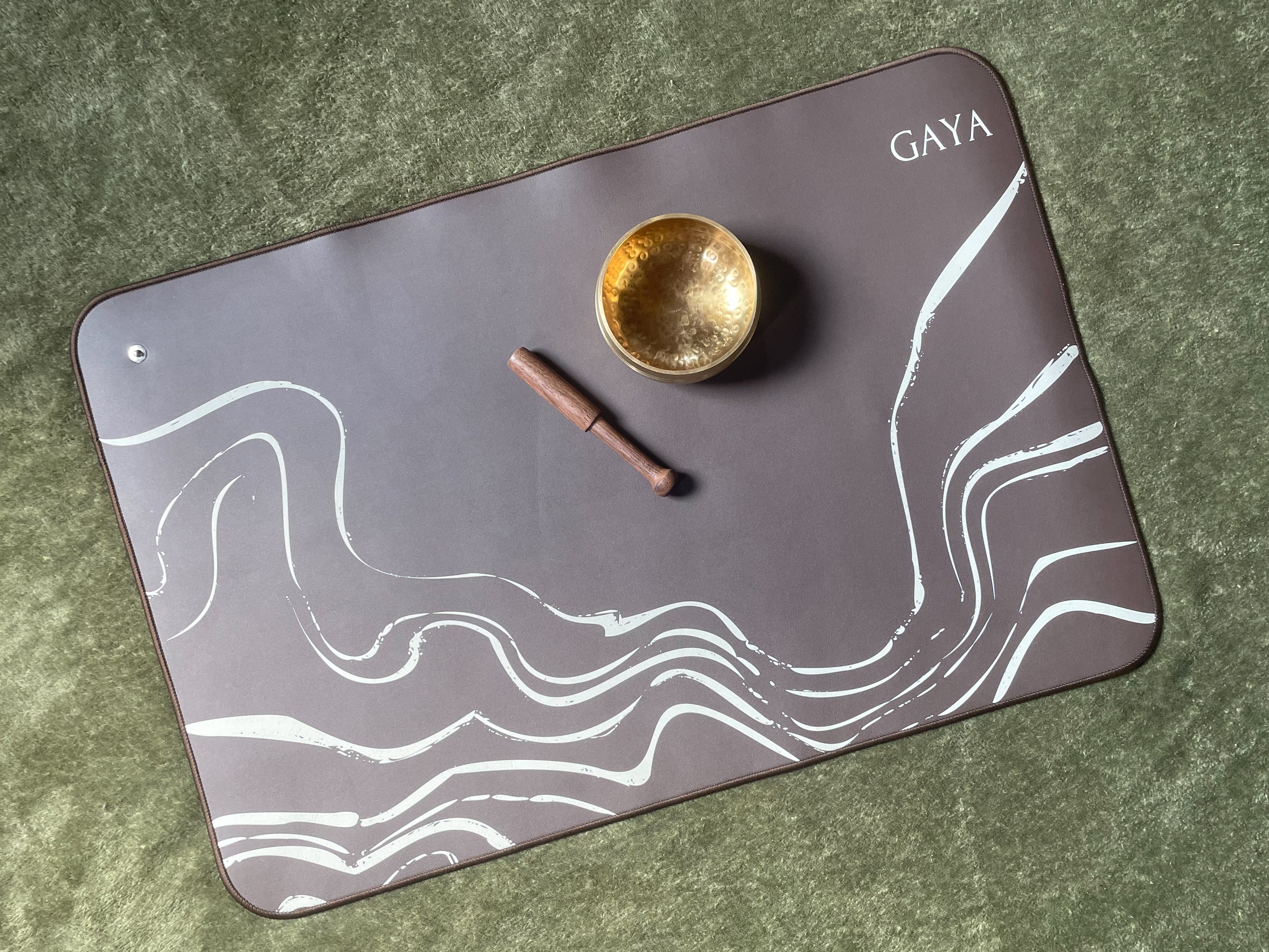 Gaya placemat with a gold bowl and wooden stick on a green surface