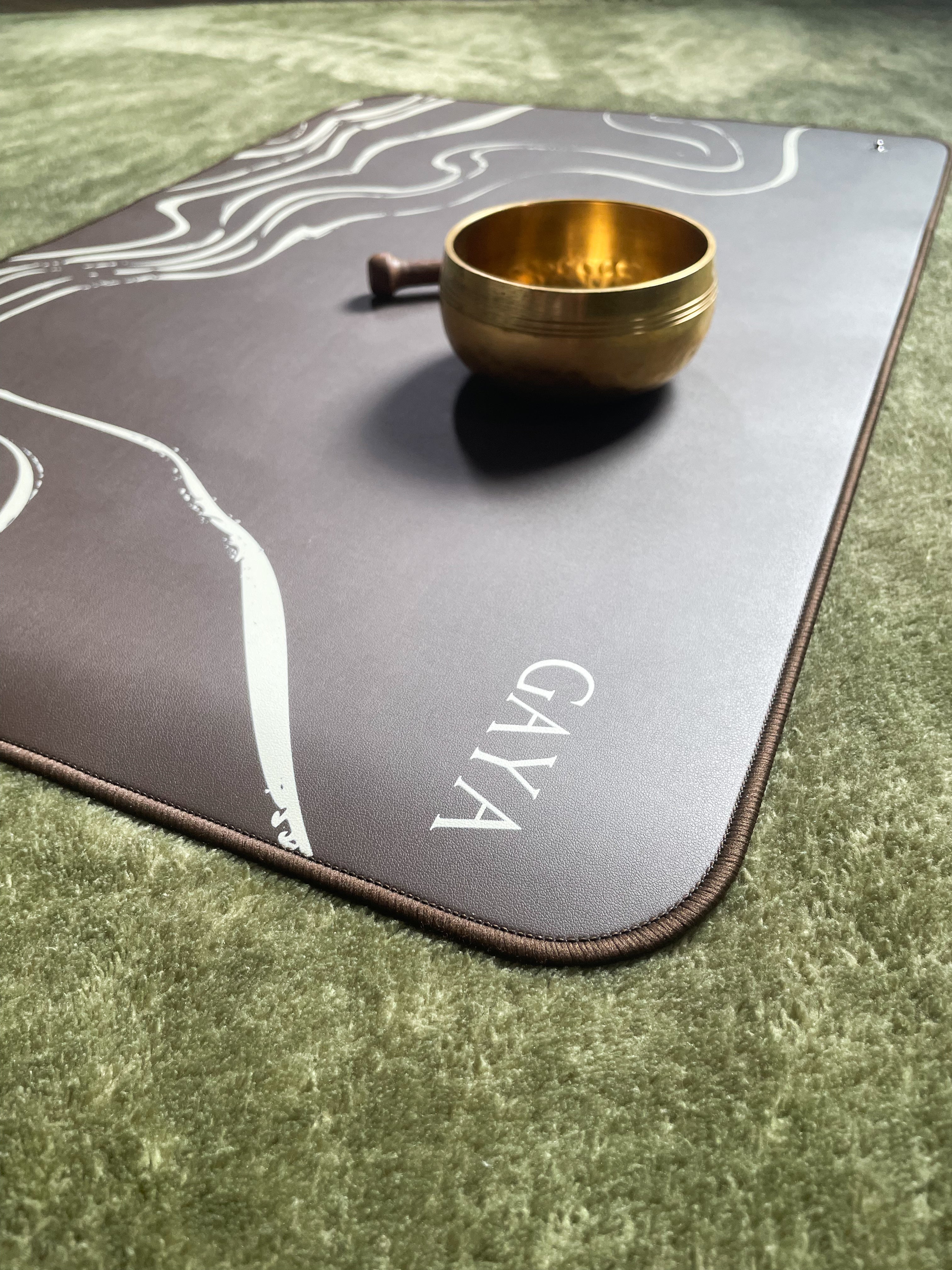 Gold singing bowl on a gray mat with 'Gaya' branding on a green grass background
