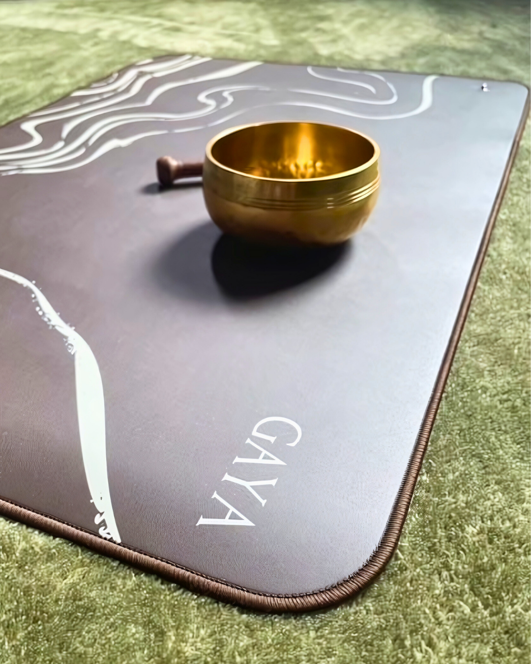 Gold singing bowl on a gray mat with 'Gaya' branding on a grassy background