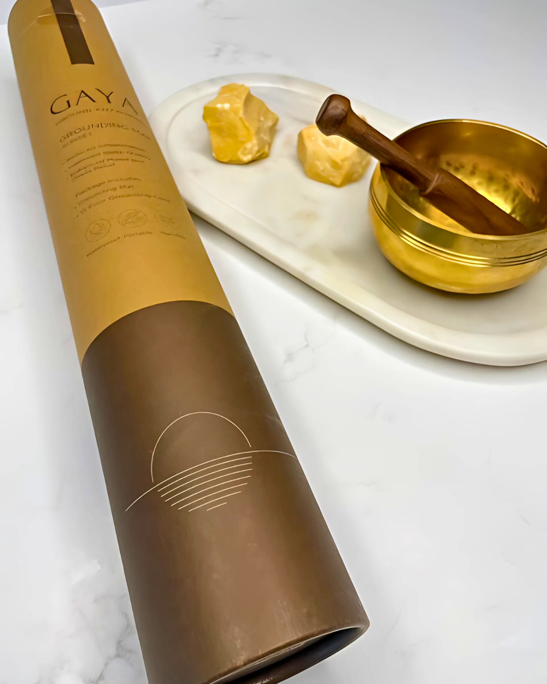 Brown cylindrical product packaging with 'GAYA' branding on a white surface with a gold bowl and stones.