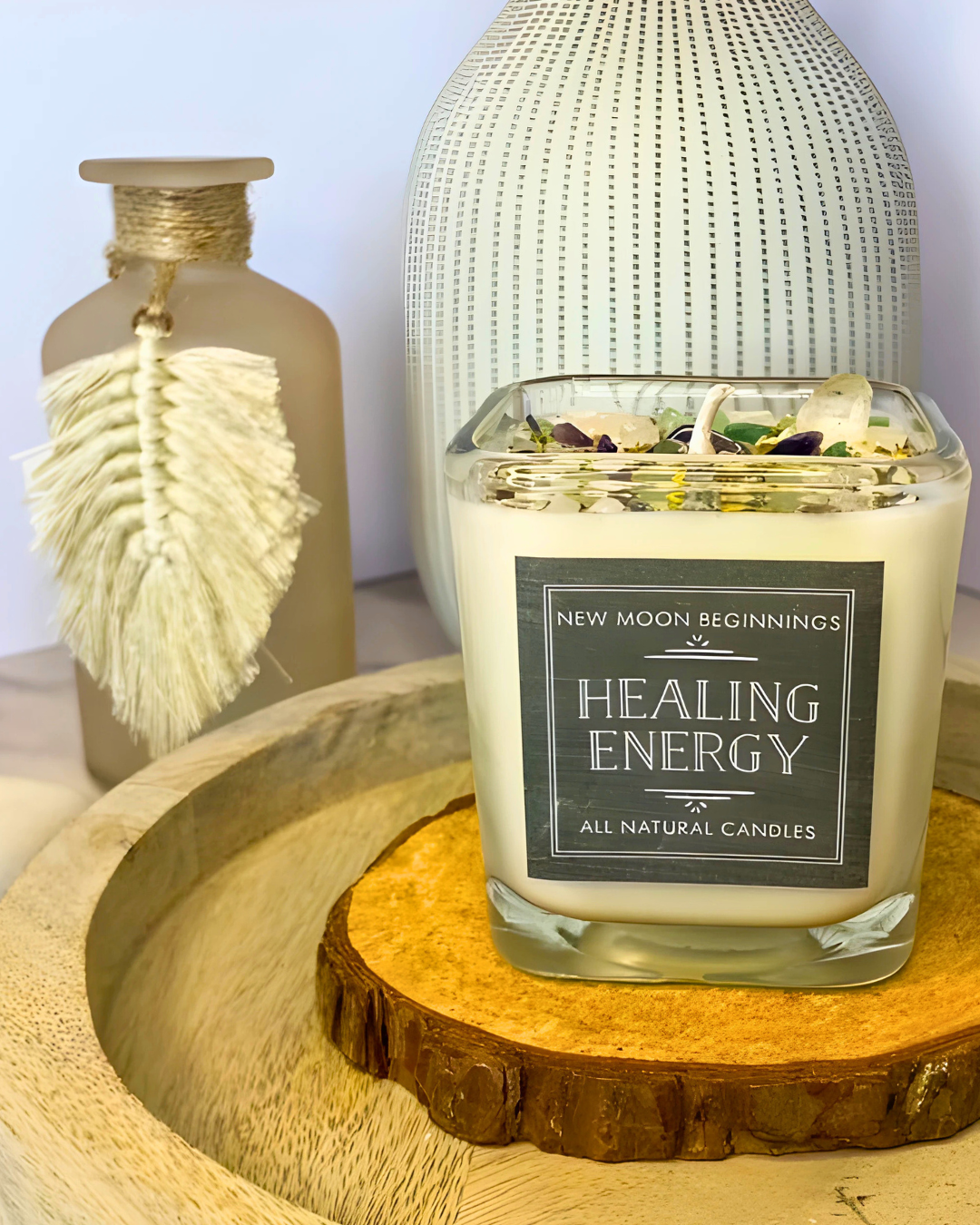 Candle labeled 'Healing Energy' by 'New Moon Beginnings' on a wooden surface with decorative bottles in the background.