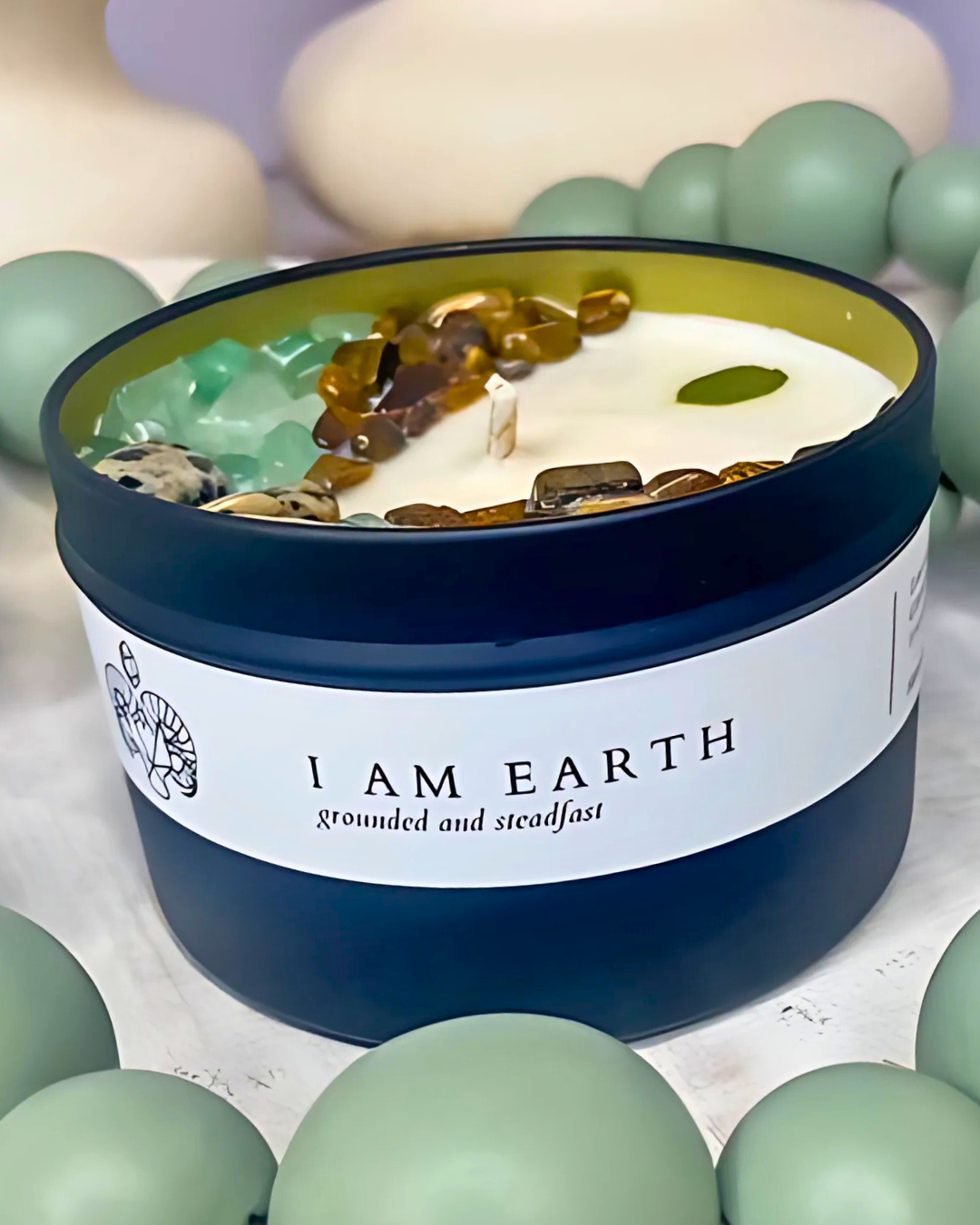 Candle in a blue container with 'I AM EARTH' label surrounded by green spherical objects.