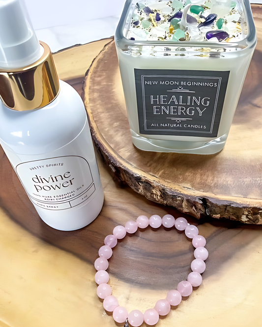 Candle labeled 'Healing Energy' with a bottle labeled 'divine power' and a pink beaded bracelet on a wooden surface.