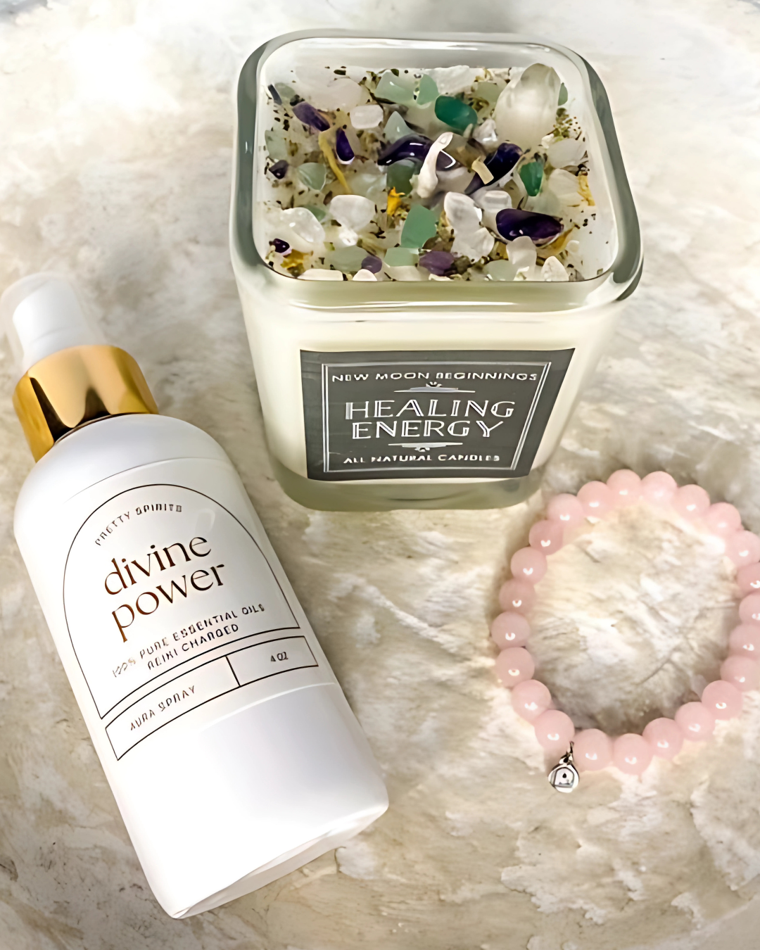 Candle labeled 'Healing Energy', bottle labeled 'divine power', and pink beaded bracelet on a textured surface.