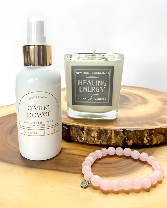 White bottle labeled 'divine power', candle labeled 'Healing Energy', and pink beaded bracelet on a wooden surface.