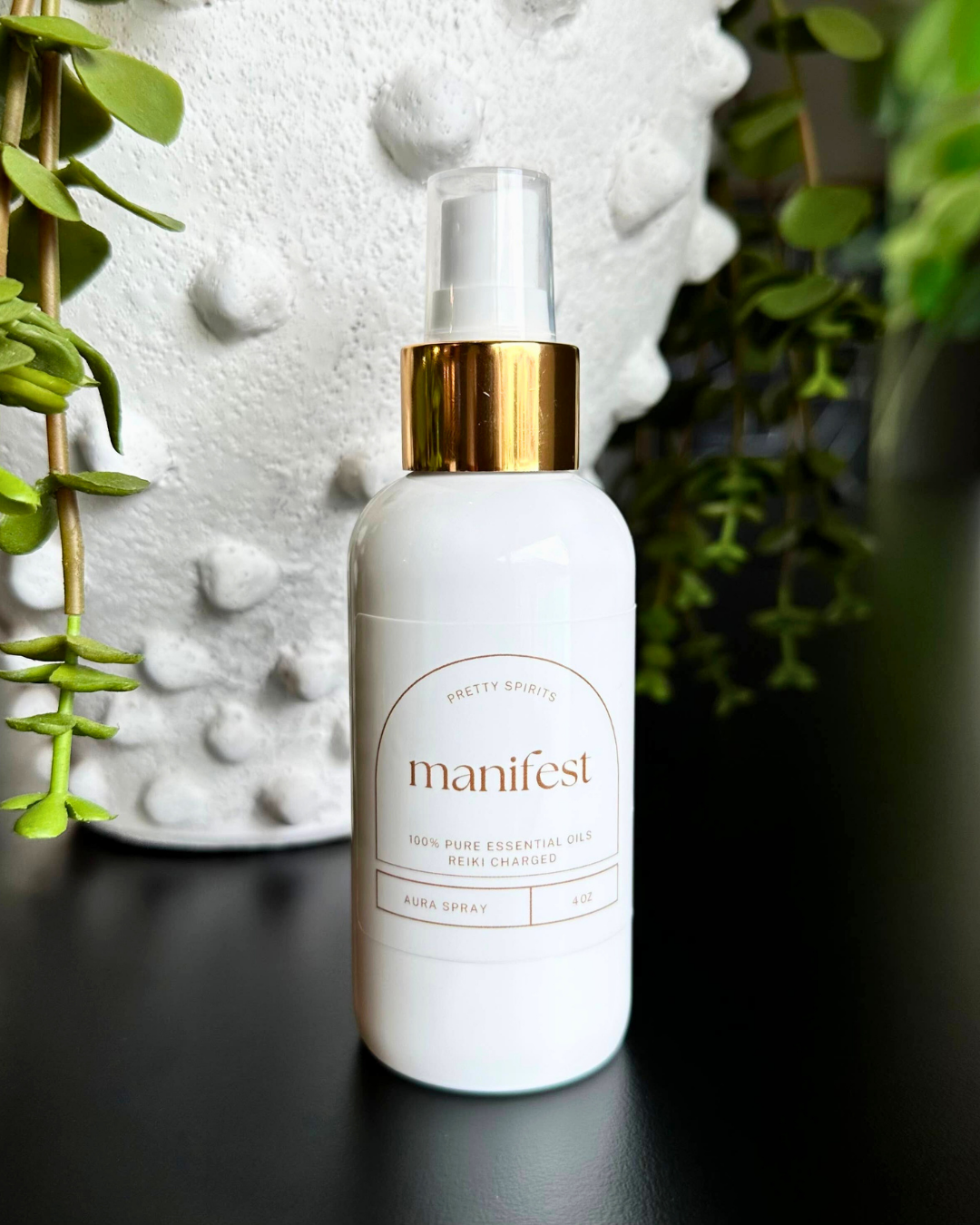 Manifest bottle with gold cap on a dark surface with greenery in the background