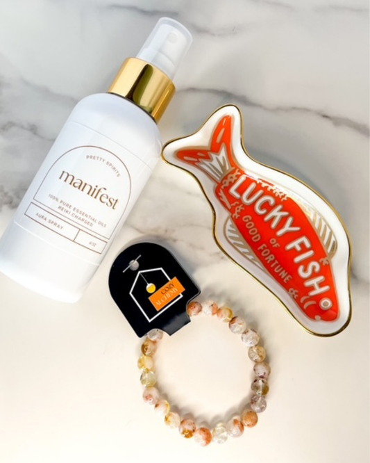 Manifest bottle, Lucky Fish jewelry, and bracelet on a marble surface