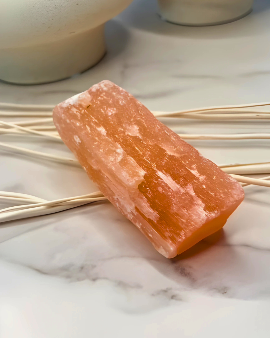 Rectangular pink crystal on a marble surface with reeds in the background