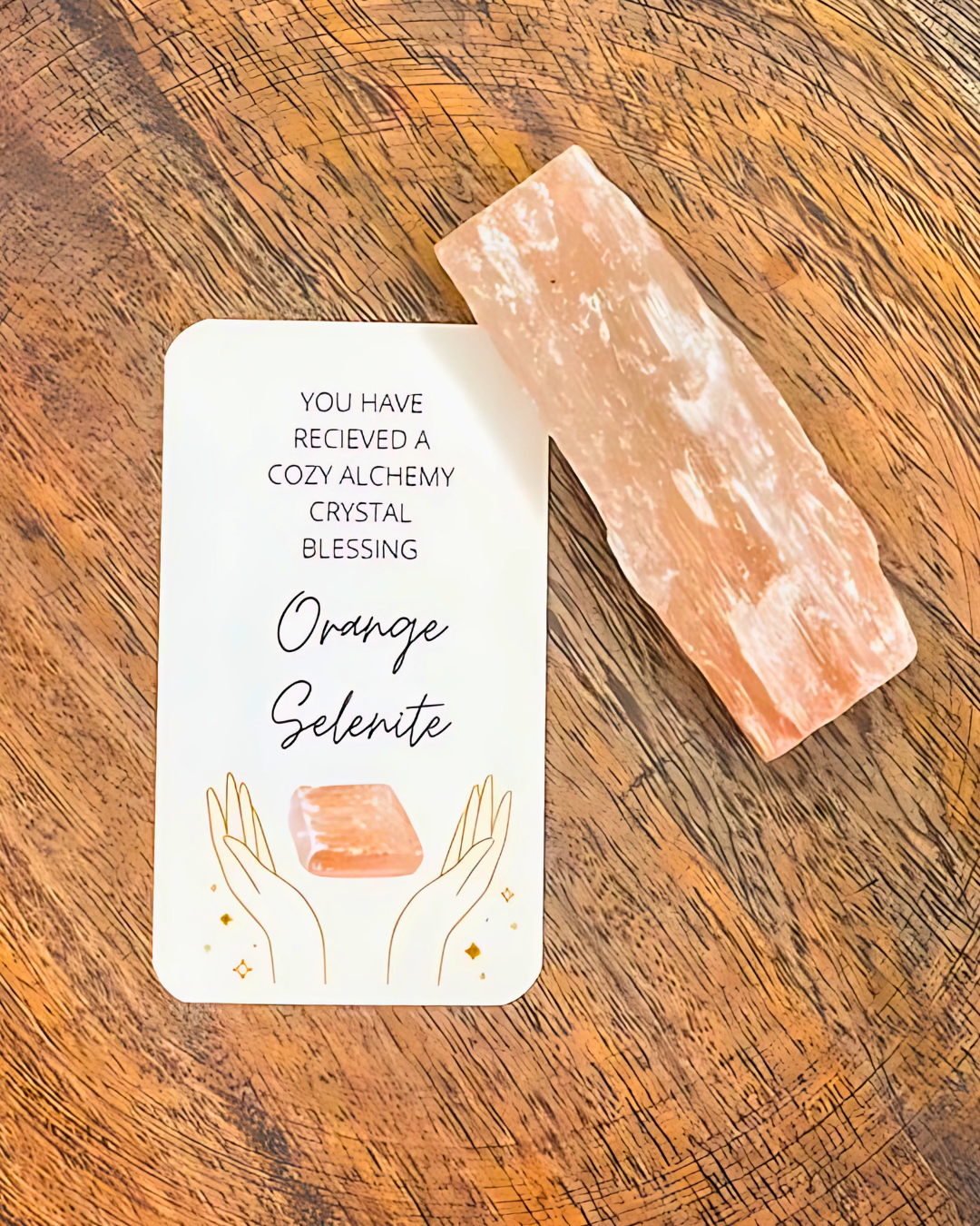 Orange selenite crystal on a wooden surface with a blessing card.