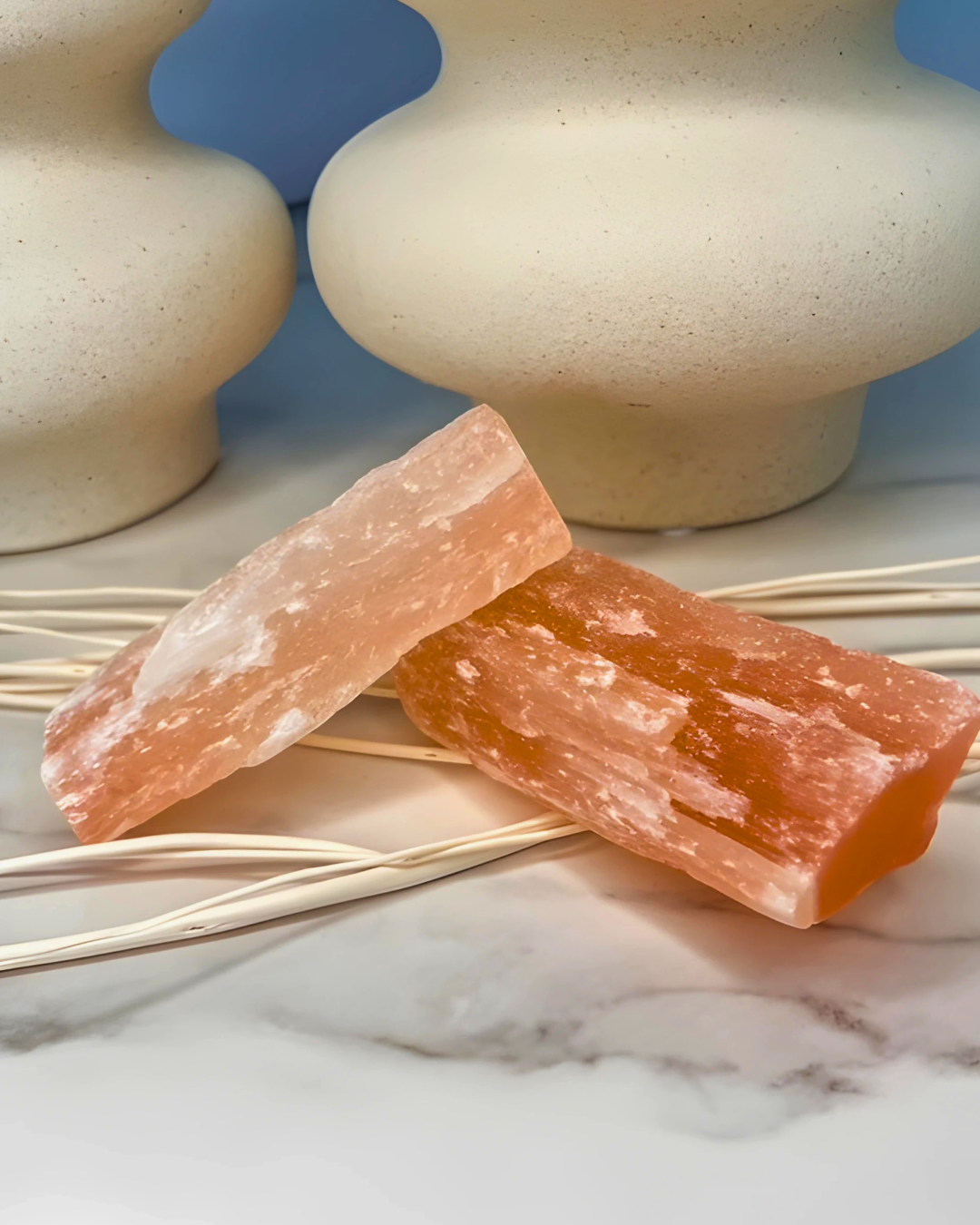 Two pink Himalayan salt blocks on a marble surface with decorative sticks and a blue background.