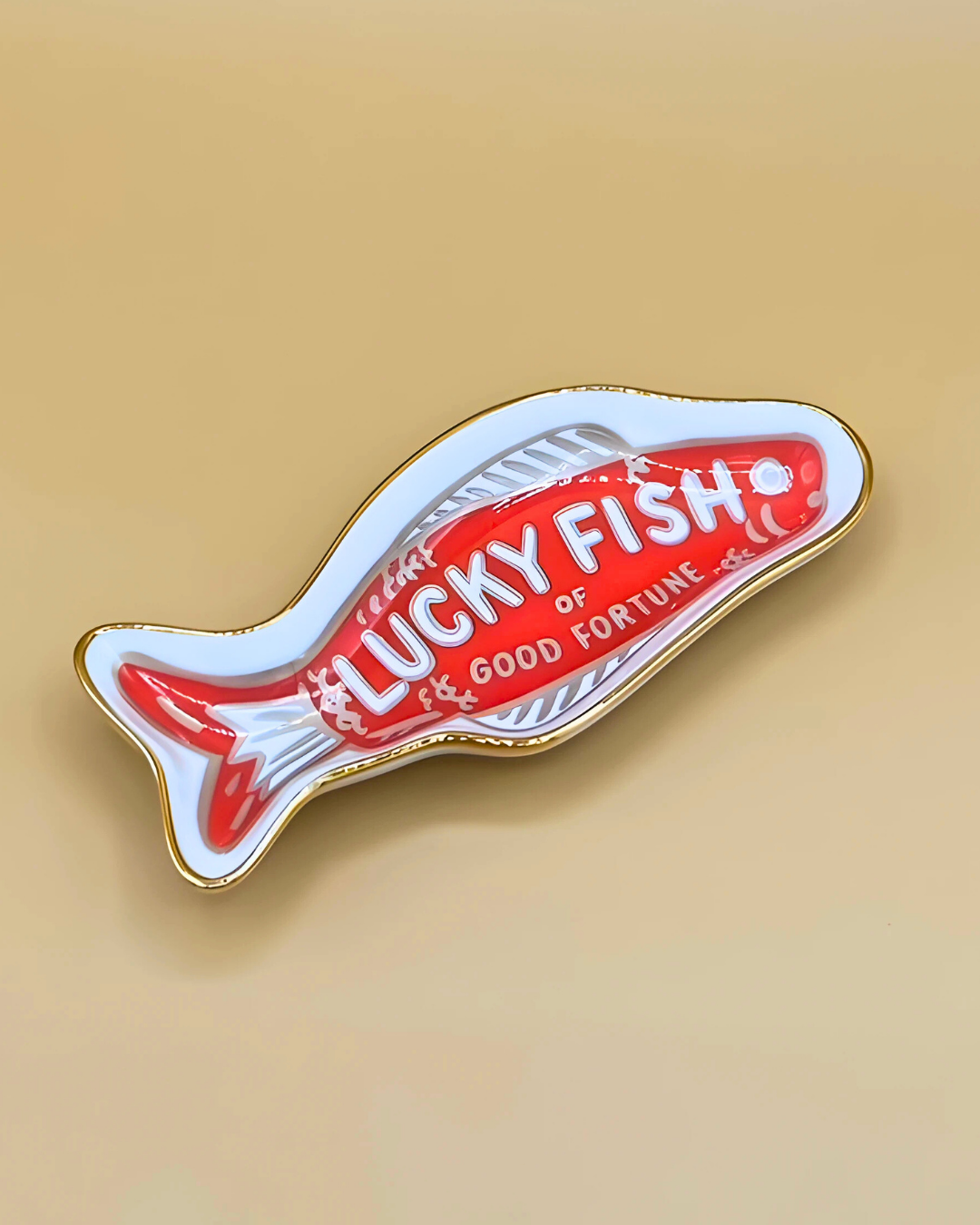 Fish-shaped enamel pin with 'Lucky Fish of Good Fortune' text on a beige background