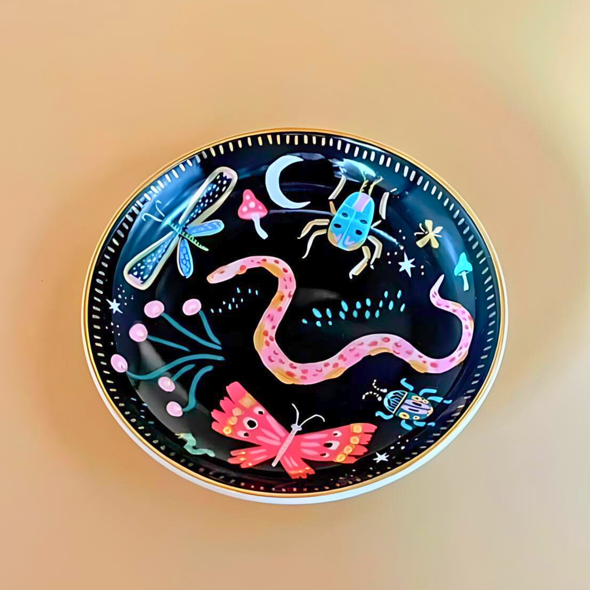 Decorative plate with colorful illustrations of a snake, butterfly, dragonfly, and other elements on a black background.