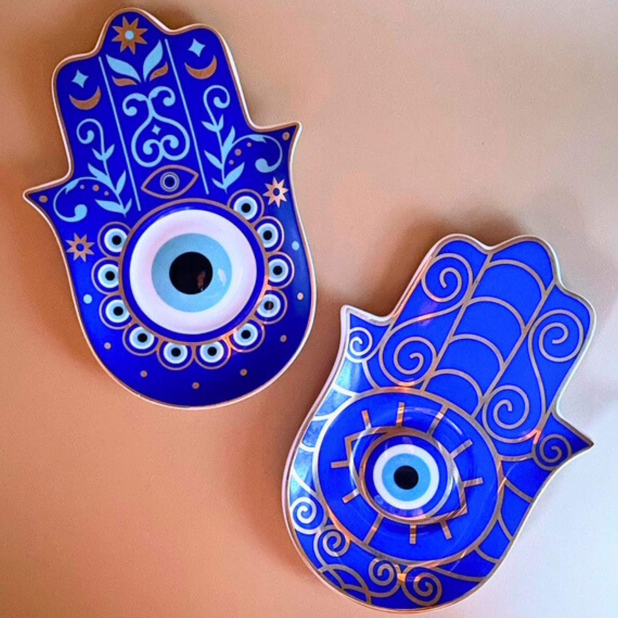 Two blue Hamsa hand pins with eye design on a beige background