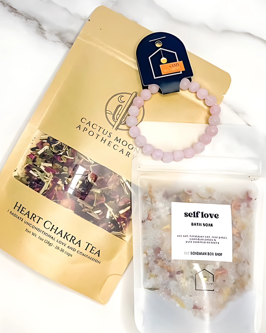 Cactus Moon Apothecary heart chakra tea package, pink beaded bracelet, and self love bath soap on a marble surface.
