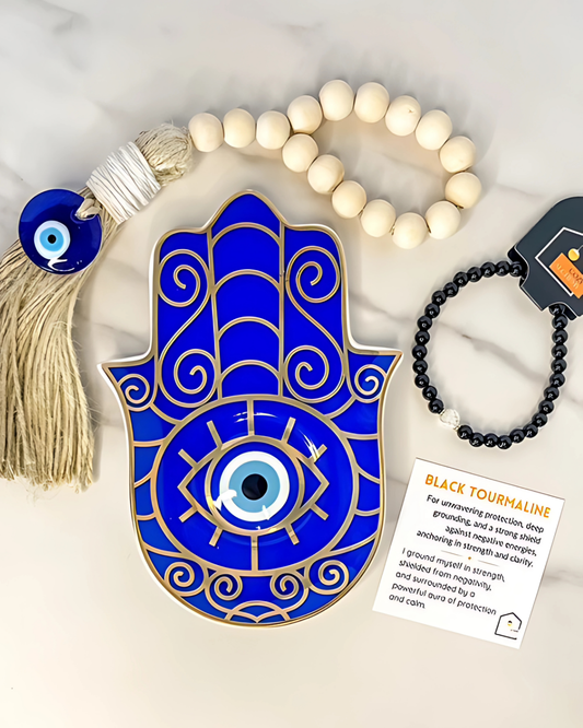 Blue Hamsa hand with tassel, white beaded necklace, and black beaded bracelet on a light background