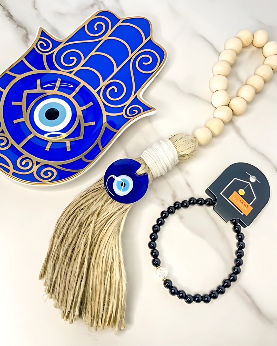 Blue Hamsa hand with tassel, evil eye charm, and prayer beads on a marble surface