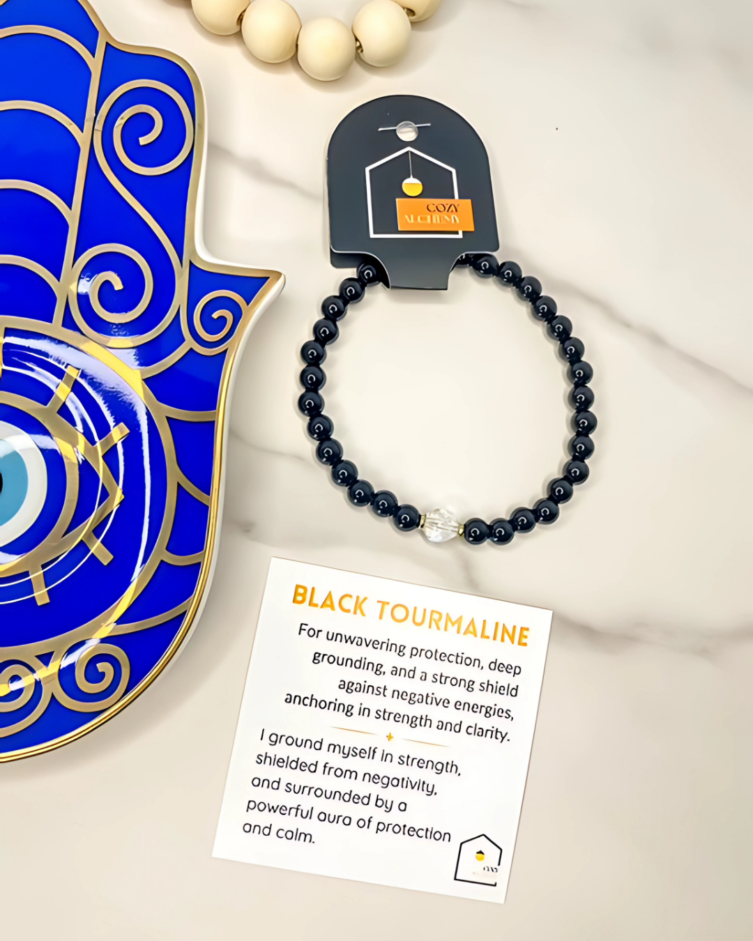 Black tourmaline bracelet on a card with product details, displayed with a decorative blue and gold object.