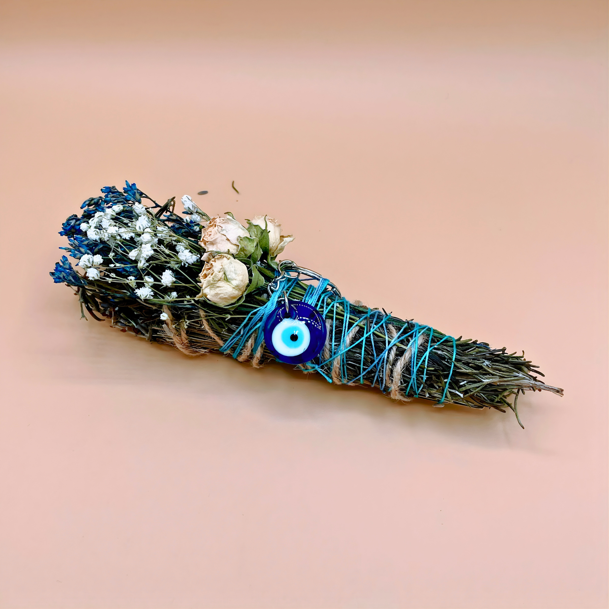 Decorative bundle with flowers and a blue evil eye charm on a beige background
