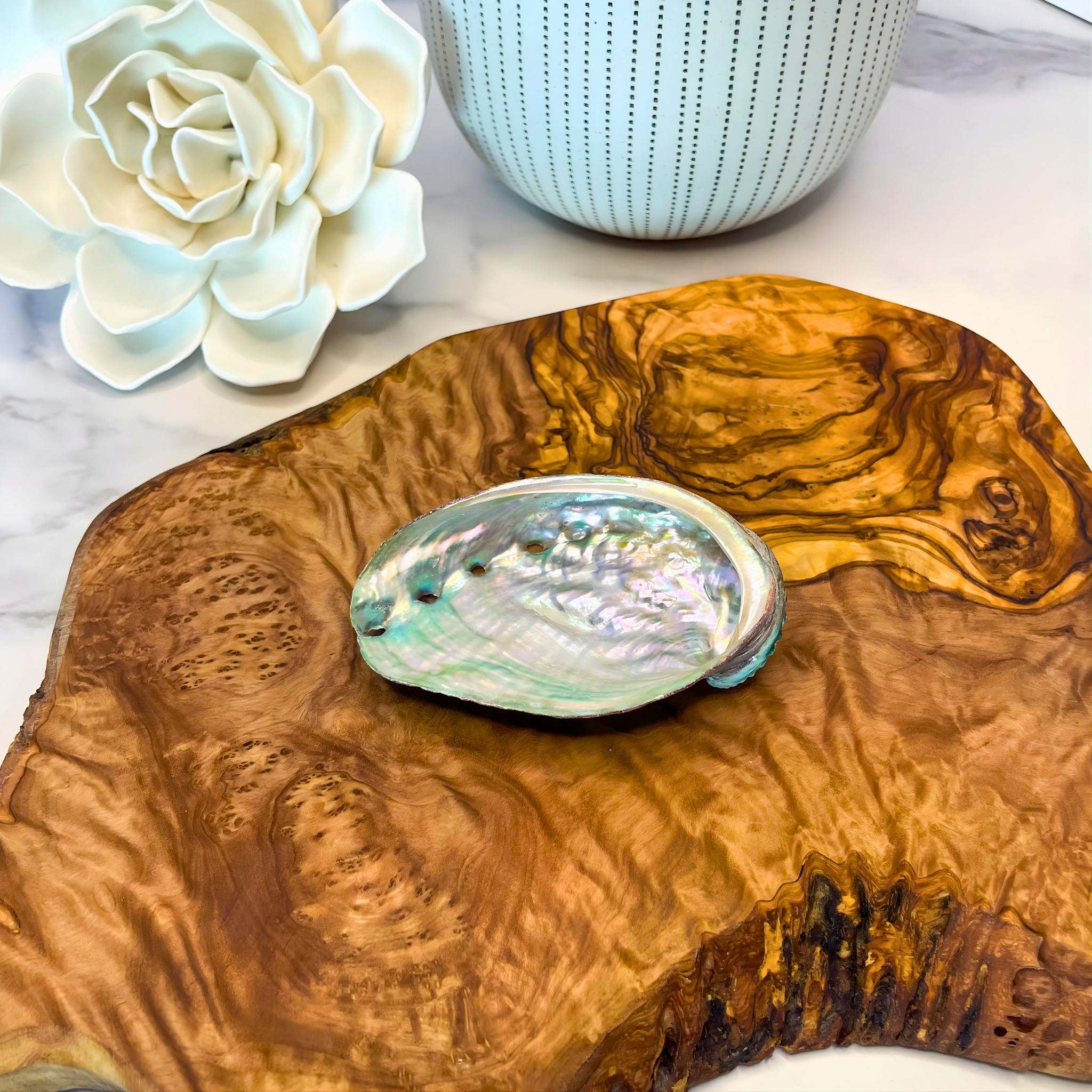 Abalone shell on a wooden surface with a white flower and ceramic item in the background