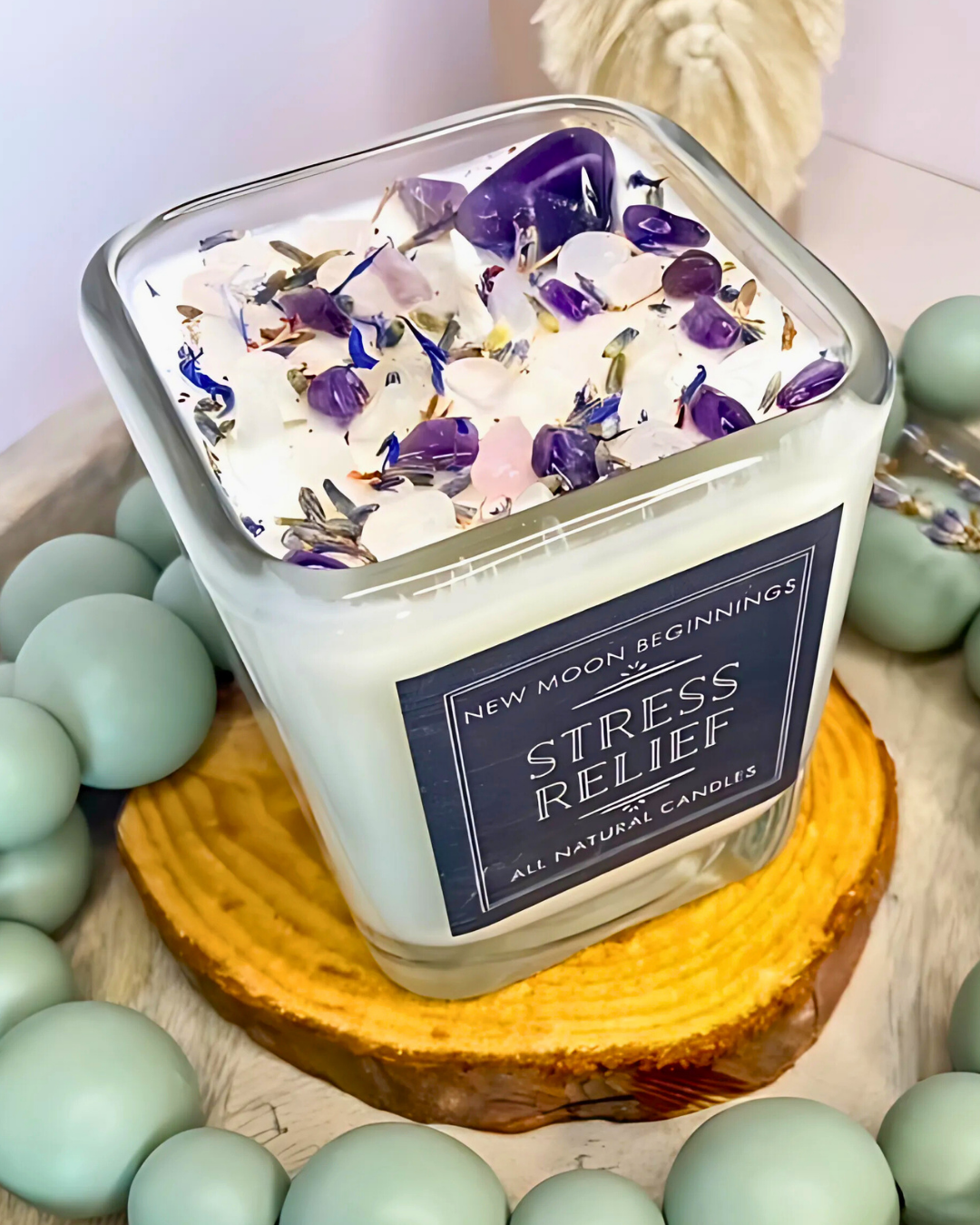Candle labeled 'Stress Relief' with floral toppings on a wooden coaster surrounded by green beads.