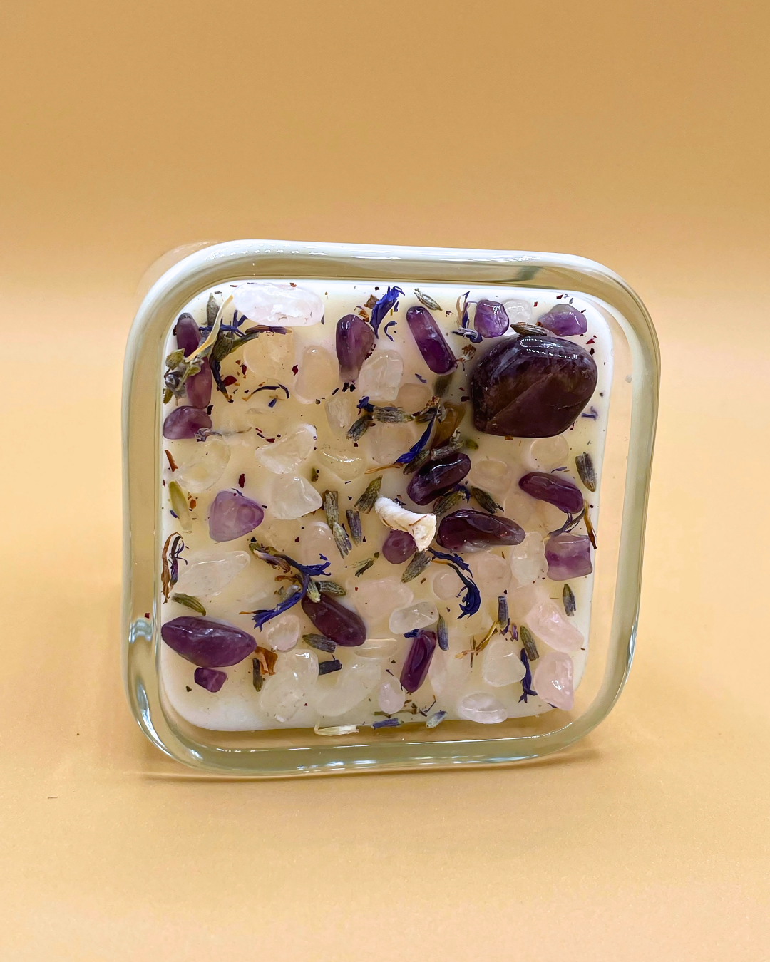Square glass container with a white substance and purple and blue bits on a beige background