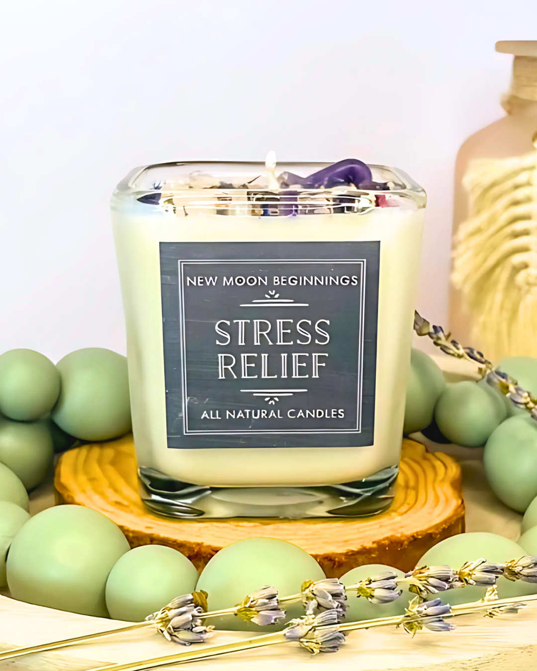Candle labeled 'Stress Relief' on a wooden stand with green spherical objects and lavender flowers in the background.
