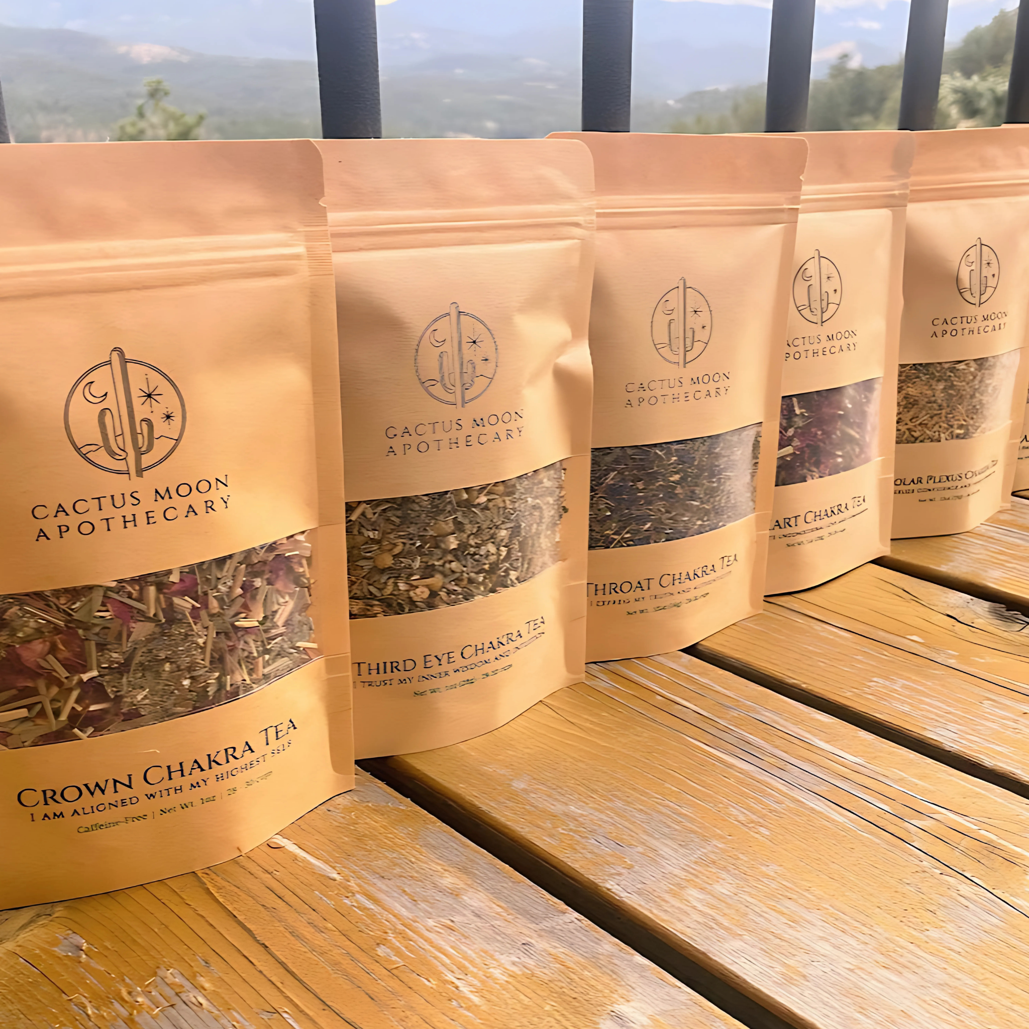 Packages of Cactus Moon Apothecary teas on a wooden surface with a scenic background