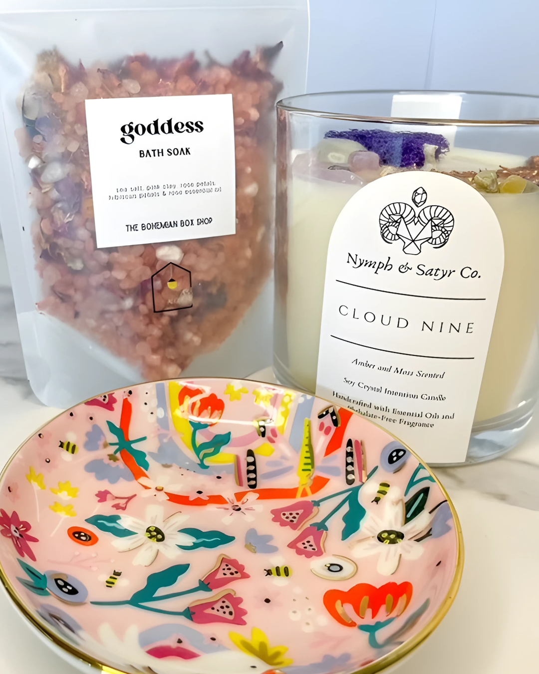Product display with 'goddess' bath soaks, 'Nymph & Satyr Co.' candle, and a decorative bowl.
