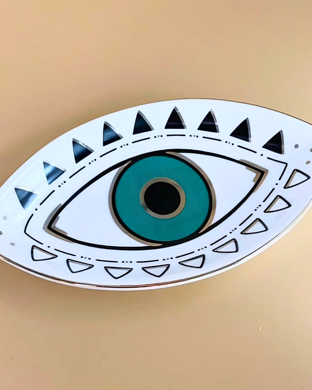 Decorative eye-shaped object with teal center and black pupil on a beige background