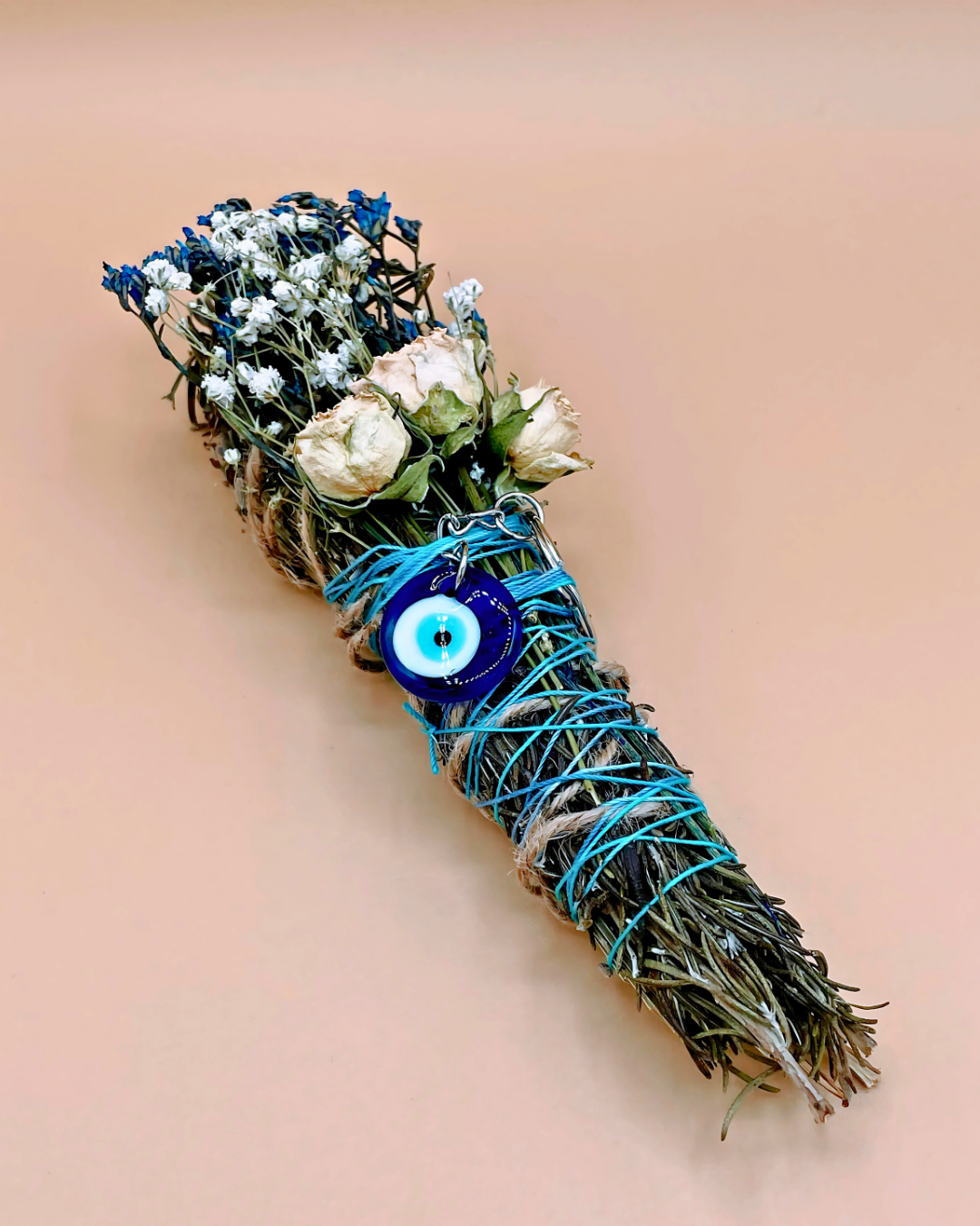 Smudge stick with flowers and blue string on a beige background