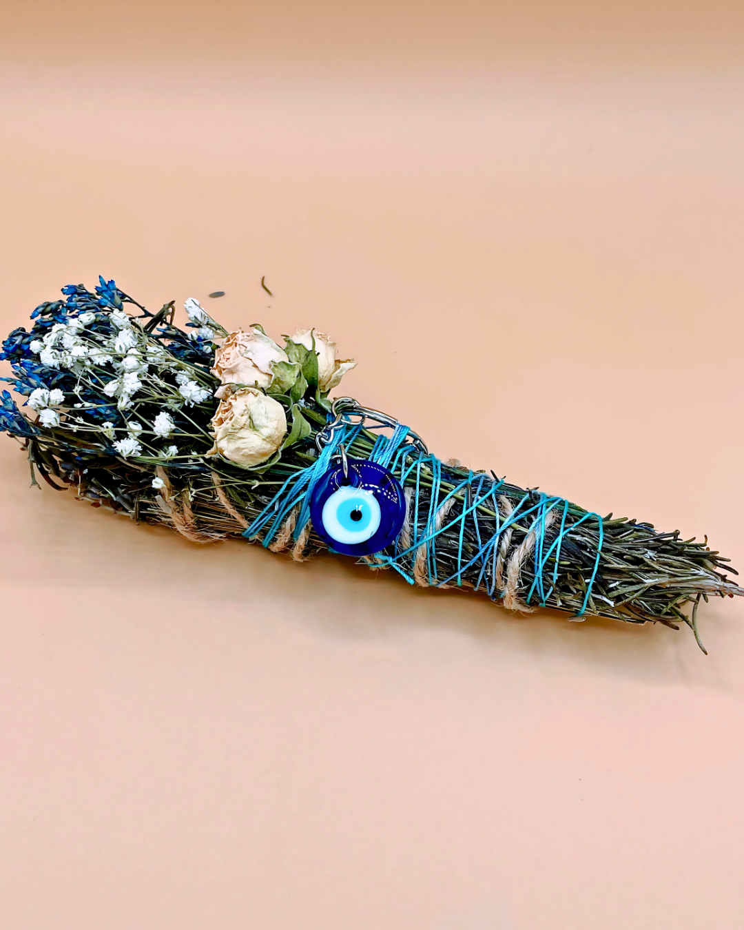 Decorative broom with flowers and a blue eye charm on a beige background