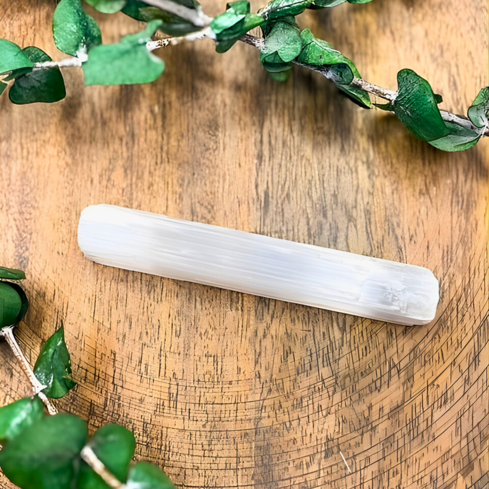 Selenite wand on a wooden surface with green leaves