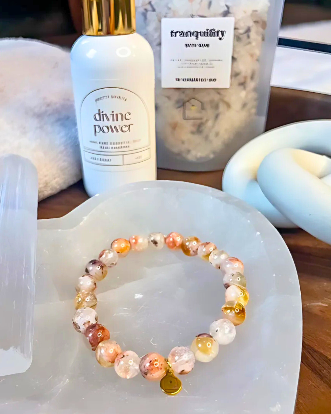 Bracelet on a white dish with 'divine power' bottle and 'tranquility' candle in the background