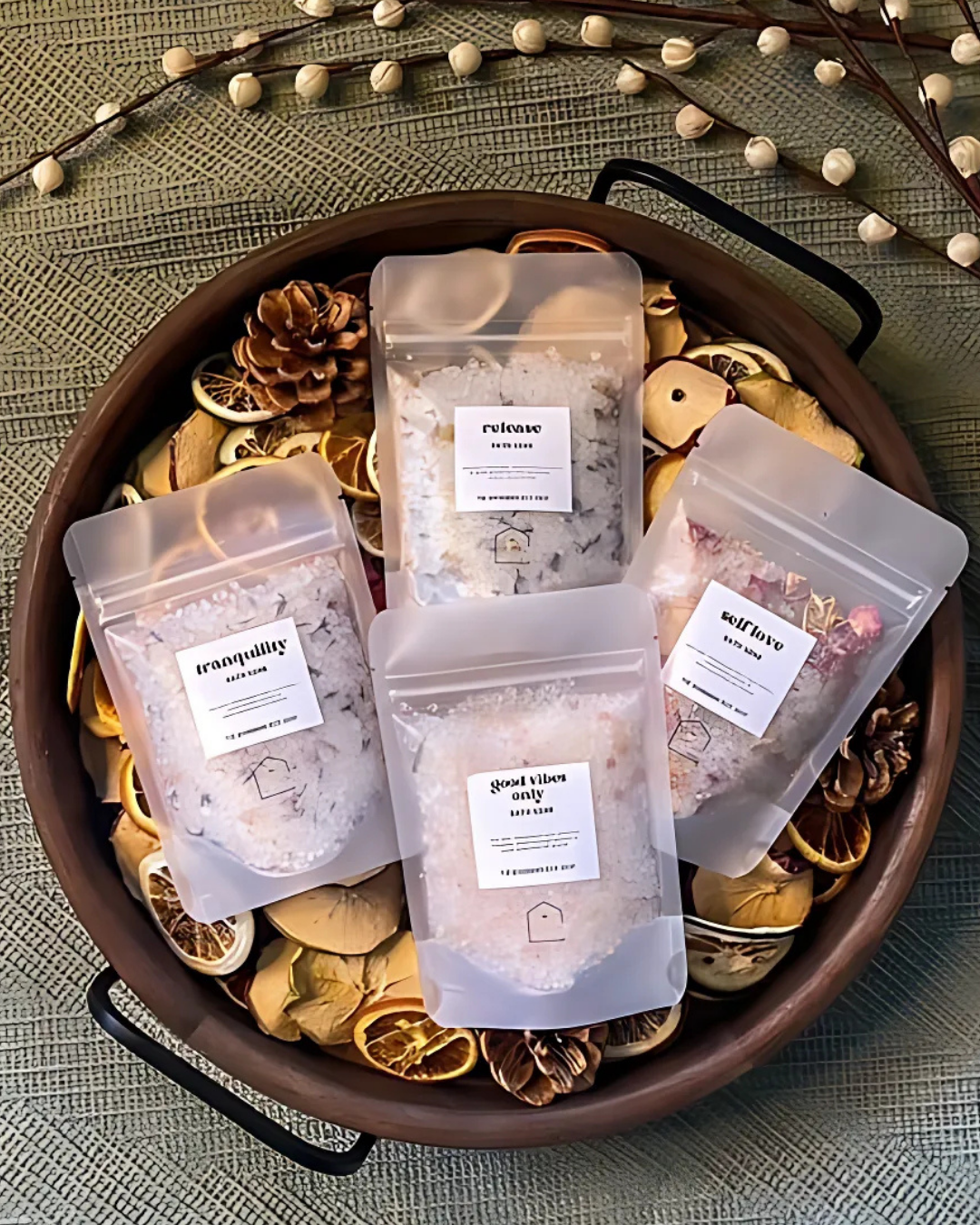 Five packages of bath salts with labels on a decorative tray with dried fruits and leaves.